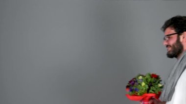 Gri arka planda bir buket çiçek tutan bir adam.