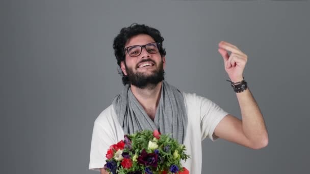 Handsome young man over grey wall holding flowers bouquet and dancing — Stock Video