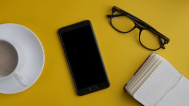 Akıllı telefon, not ve kahve sarı arka plan üzerinde. Sinemagrafı.