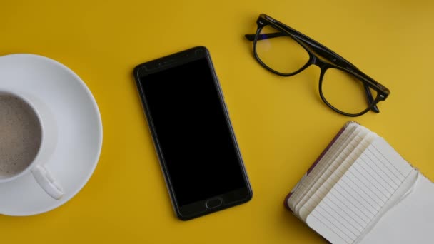 Smartphone, Σημείωση και καφέ σε κίτρινο φόντο. Cinemagraph. — Αρχείο Βίντεο