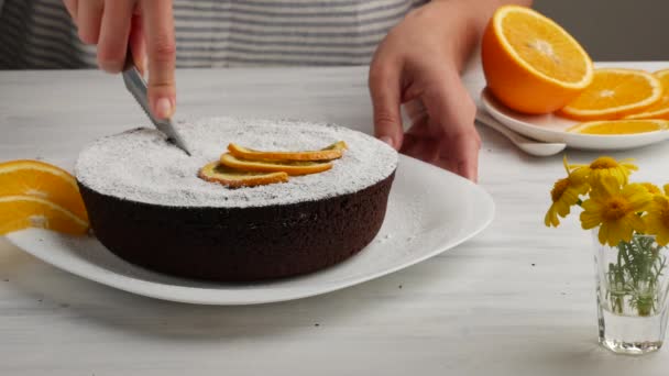 Mujer cortando pastel de chocolate Decorado con rodajas de naranja . — Vídeos de Stock