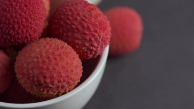 Gri bir arka plan üzerinde beyaz kase taze lychee döndürün.