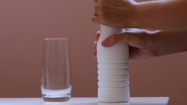 Versare lo yogurt da una bottiglia bianca in un bicchiere su uno sfondo rosa — Video Stock