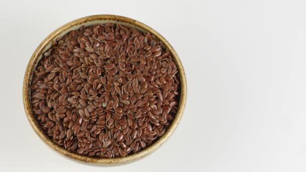 Střídání lněných semen v keramickém míse na bílém pozadí. — Stock video