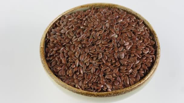 Rotação de sementes de linho em tigela de cerâmica sobre fundo branco . — Vídeo de Stock