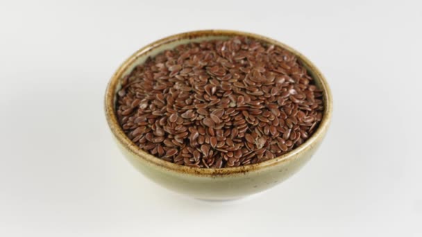 Rotación de semillas de lino en cuenco de cerámica sobre fondo blanco . — Vídeos de Stock