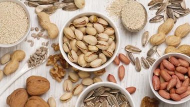 Assortment of nuts and seeds in white saucers on a white background.