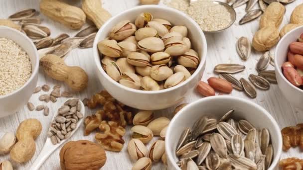 Assortment of nuts and seeds in white saucers on a white background. — Stock Video