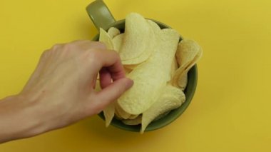 Sarı arka planda seramik kasede patates cipsi. Üst görünüm.