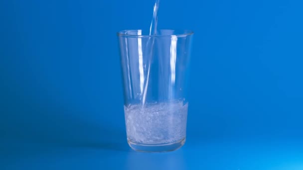 Giet koolzuurhoudend mineraalwater in een glas op een blauwe ondergrond. — Stockvideo