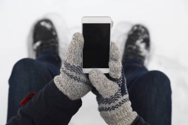 Adam boş ekran akıllı telefon tutarak yün eldiven ver. Yakın çekim