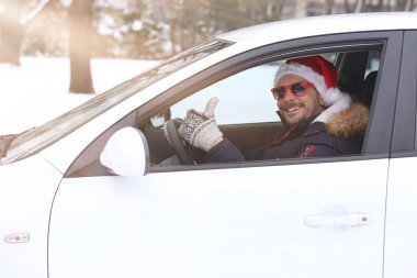 Noel Baba şapkası ve kar ve güneşli dan zevk kadar başparmak ile araç sürücüsü portresi. Tatil ve kış konsepti.
