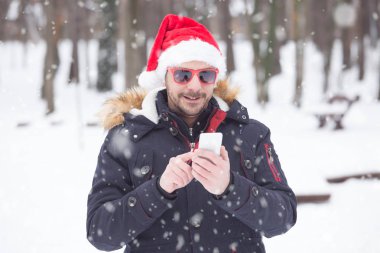 Santa şapka ve güneş gözlüğü kar gün sms gönderme ile genç adam portresi. Kış konsepti