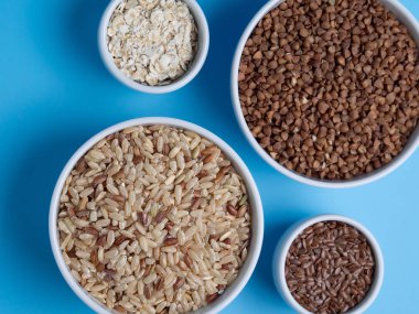 mavi bir arka plan üzerinde beyaz su bardağı kahverengi pirinç, buğday, keten ve yulaf gevreği