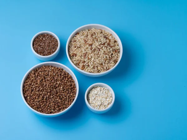 mavi bir arka plan üzerinde beyaz su bardağı kahverengi pirinç, buğday, keten ve yulaf gevreği