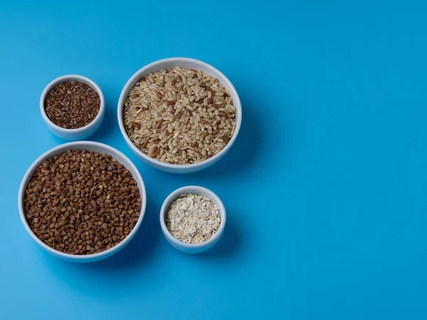 mavi bir arka plan üzerinde beyaz su bardağı kahverengi pirinç, buğday, keten ve yulaf gevreği