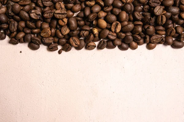 Roasted coffee beans in bulk on a light pink background. dark co