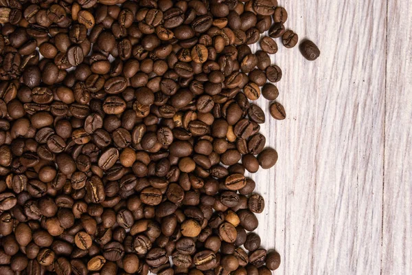 Жареные кофейные зерна оптом на светлом деревянном фоне. темные — стоковое фото