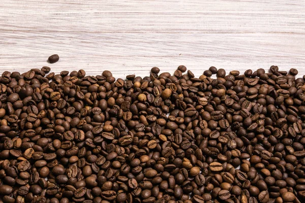 Kavrulmuş kahve çekirdekleri hafif ahşap arka plan üzerinde toplu olarak. karanlık 