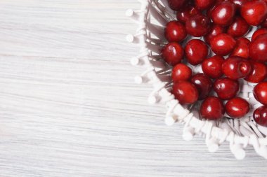 Beyaz ahşap masada beyaz bir sepet kırmızı tatlı kiraz