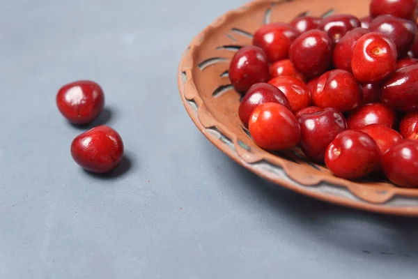 Ciliegia dolce rossa in un piatto di argilla su un tavolo grigio — Foto Stock