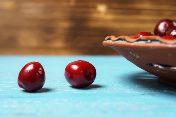 Turkuaz ahşap masada bir kil plaka kırmızı tatlı kiraz