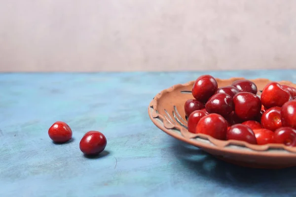 Ciliegia dolce rossa in un piatto di argilla su un tavolo turchese — Foto Stock