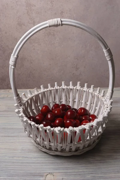 Cerezas rojas dulces en una canasta blanca sobre una mesa de madera blanca — Foto de Stock