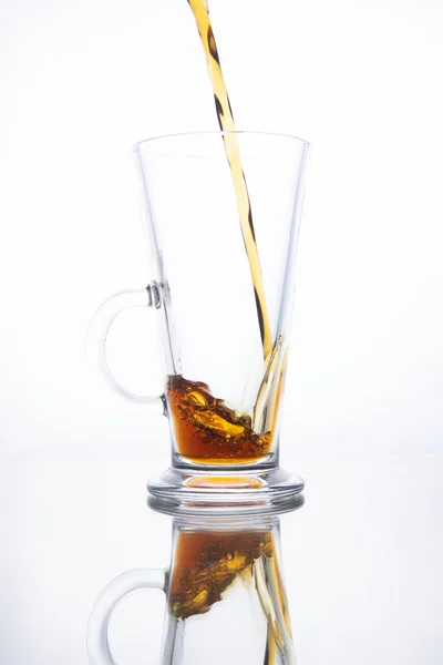 La cerveza oscura se vierte en una taza vacía sobre un fondo blanco. Sp —  Fotos de Stock