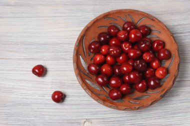 Beyaz ahşap masada bir kil çanak kırmızı tatlı kiraz