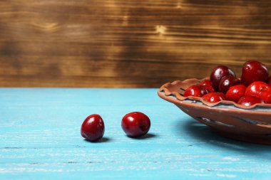 Turkuaz ahşap masada bir kil plaka kırmızı tatlı kiraz