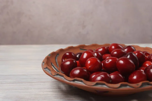 Ciliegie dolci rosse in un piatto di argilla su un tavolo di legno bianco — Foto Stock