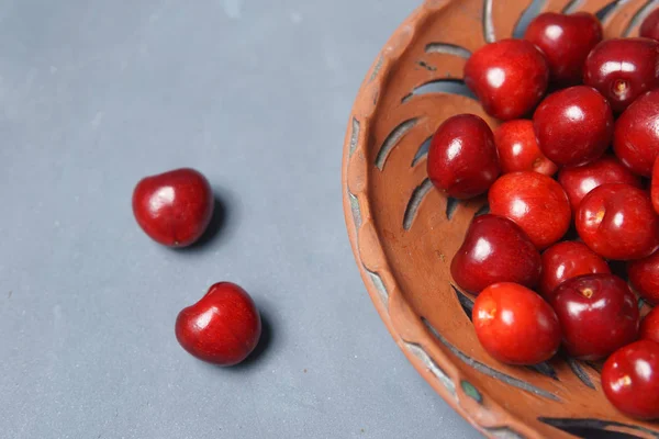 Ciliegia dolce rossa in un piatto di argilla su un tavolo grigio — Foto Stock