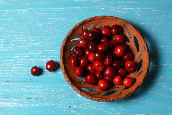 Turkuaz ahşap masada bir kil plaka kırmızı tatlı kiraz