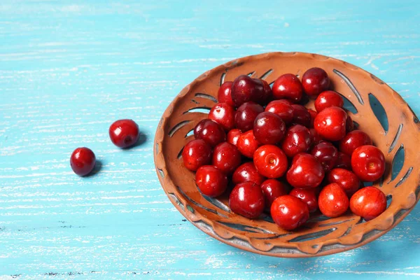 Ciliegia dolce rossa in un piatto di argilla su un tavolo di legno turchese — Foto Stock