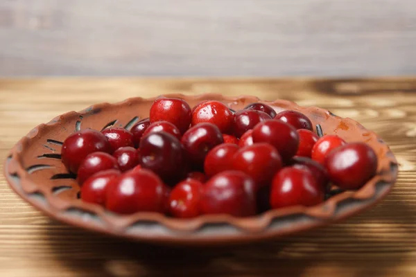 Red sweet cherry in a clay plate on a wooden table — Stock Photo, Image