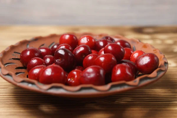 Ciliegia dolce rossa in un piatto di argilla su un tavolo di legno — Foto Stock
