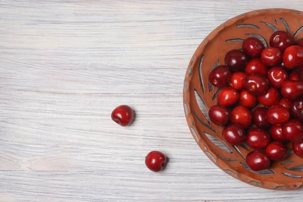 Beyaz ahşap masada bir kil çanak kırmızı tatlı kiraz