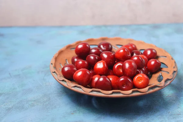 Ciliegia dolce rossa in un piatto di argilla su un tavolo turchese — Foto Stock