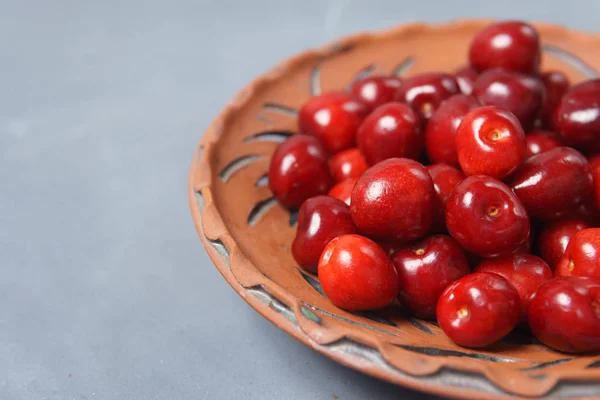 Czerwona słodka wiśnia w glinianych płytce na szarym stole — Zdjęcie stockowe