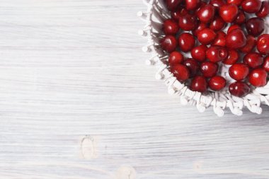 Beyaz ahşap masada beyaz bir sepet kırmızı tatlı kiraz