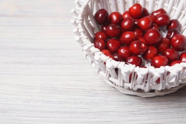 Beyaz ahşap masada beyaz bir sepet kırmızı tatlı kiraz