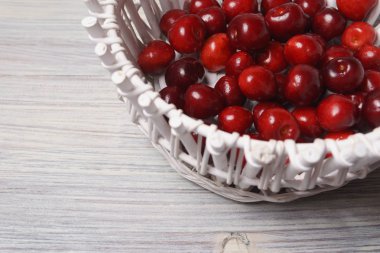 Beyaz ahşap masada beyaz bir sepet kırmızı tatlı kiraz