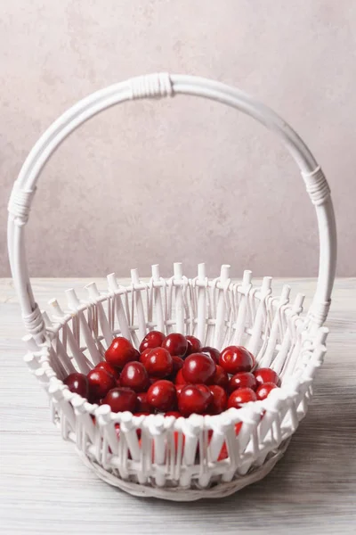 Beyaz ahşap masada beyaz bir sepet kırmızı tatlı kiraz