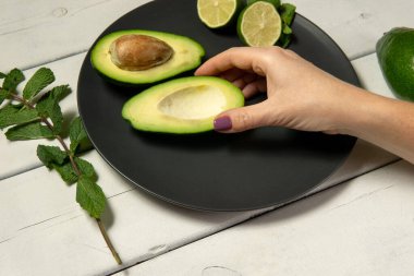 Beyaz ahşap bir arka planda çiğ avokado ve limon hazırlayan kadın.