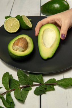 Beyaz ahşap bir arka planda çiğ avokado ve limon hazırlayan kadın.