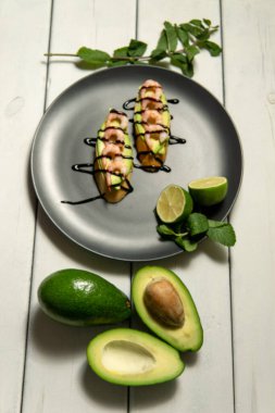 Beyaz ahşap arka planda karides, avokado ve limonlu bruschetta.