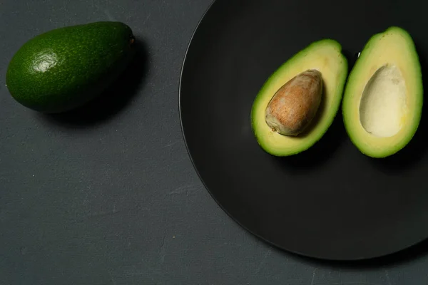 Frische, rohe Avocado in Scheiben auf einem schwarzen Teller — Stockfoto