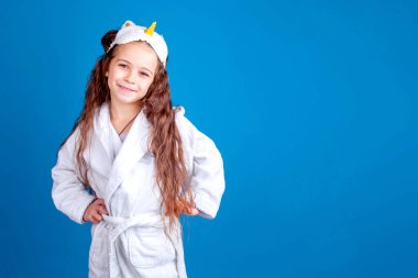 Beyaz bornozlu ve maskeli bir kız stüdyoda mavi arka planda.