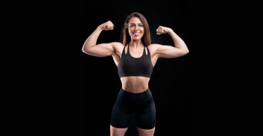 Stüdyoda siyah arka planda poz veren kadın sporcu.